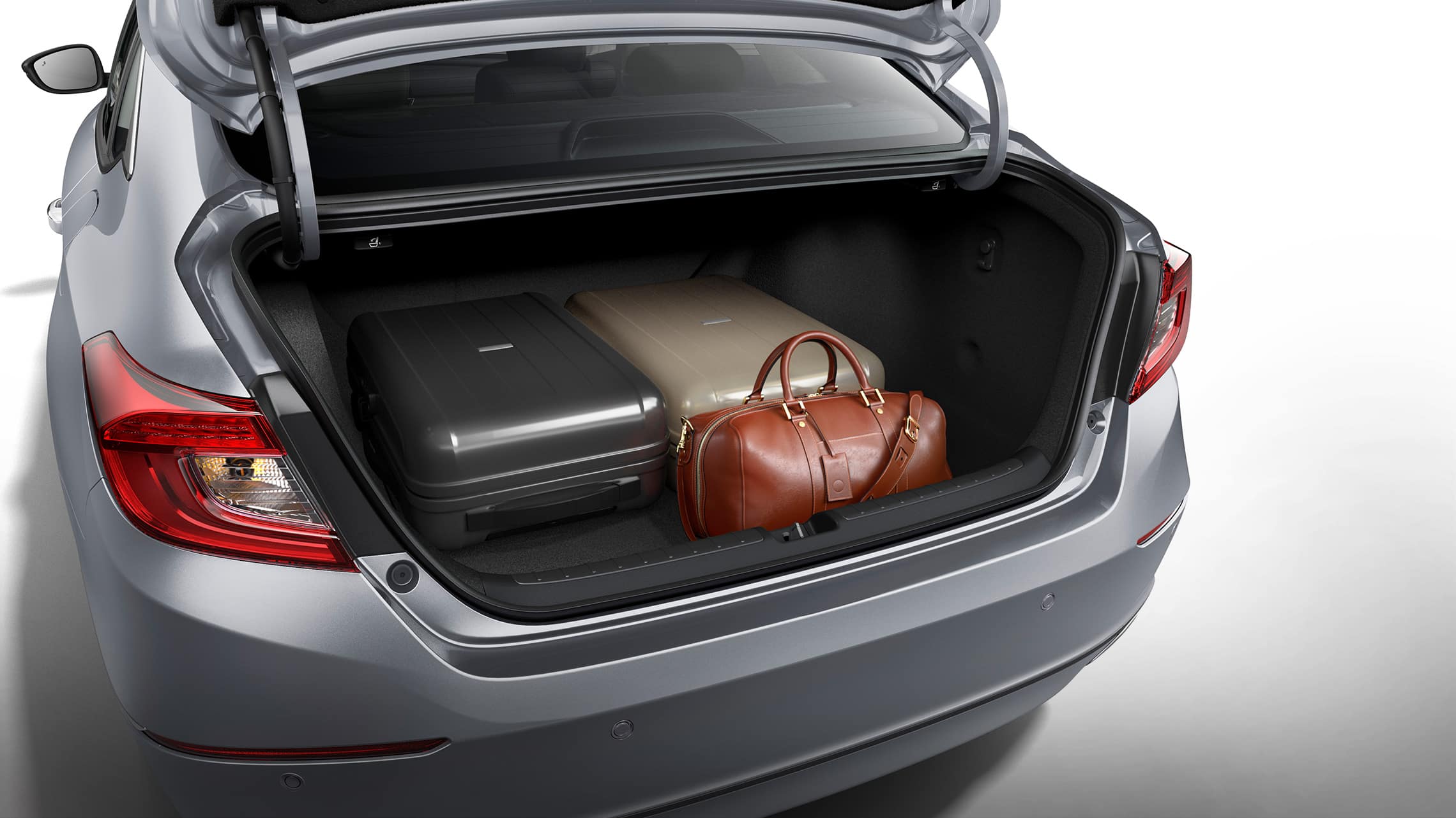 Rear view of the 2021 Accord Hybrid, shown in Lunar Silver Metallic, with the trunk open and with stored luggage displayed.