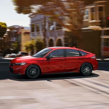 2026 Honda Civic Hatchback Sport Hybrid in Rallye Red profile driving on a city street (Compact Hatchback).
