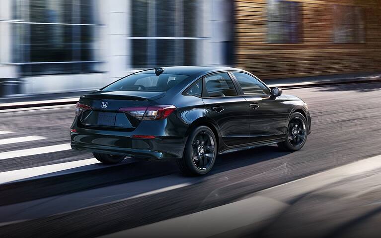 2027 Honda Civic Sedan Sport Hybrid in Crystal Black Pearl rear three-quarter view driving on a city street (Compact Sedan)